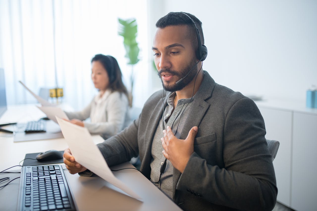 Businessman working at a call center desk, wearing a headset and reading documents.